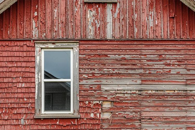 Severely peeling and weathered red paint on old wooden siding, showing damage from using the wrong option instead of the best exterior paint for wood.