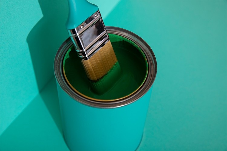 Paint brush dipping into high-quality coating used for longest lasting exterior paint applications.